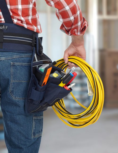Electrician man with drill and wire cable over construction background.